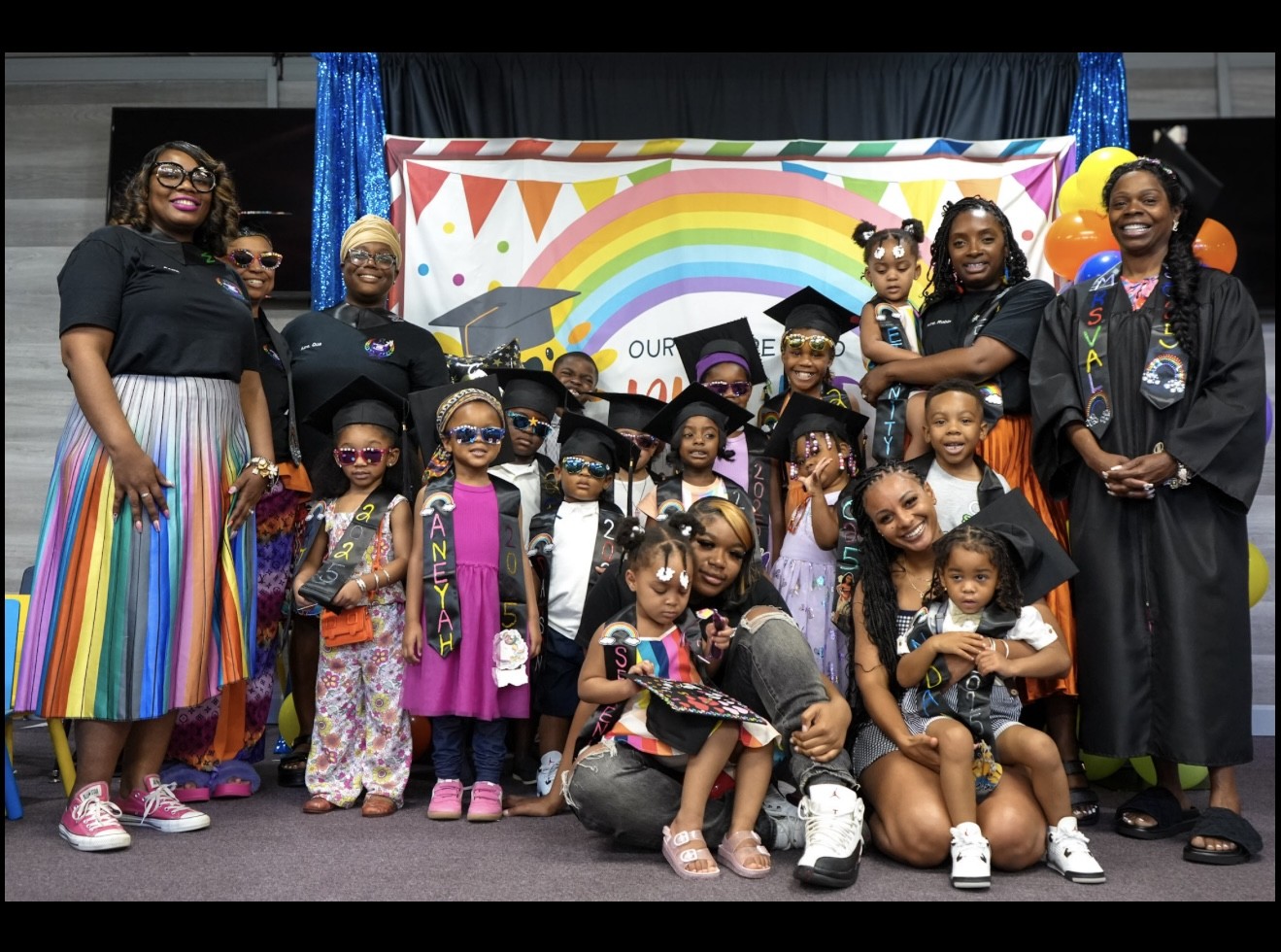 Graduates, families and Academy staff together in front of the graduation backdrop